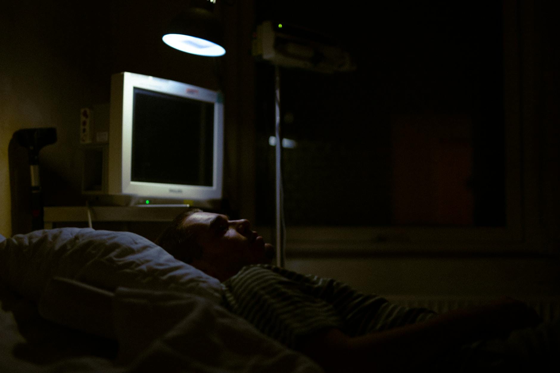 Mężczyzna leży na szpitalnym łóżku w przyciemnionej sali z aparaturą