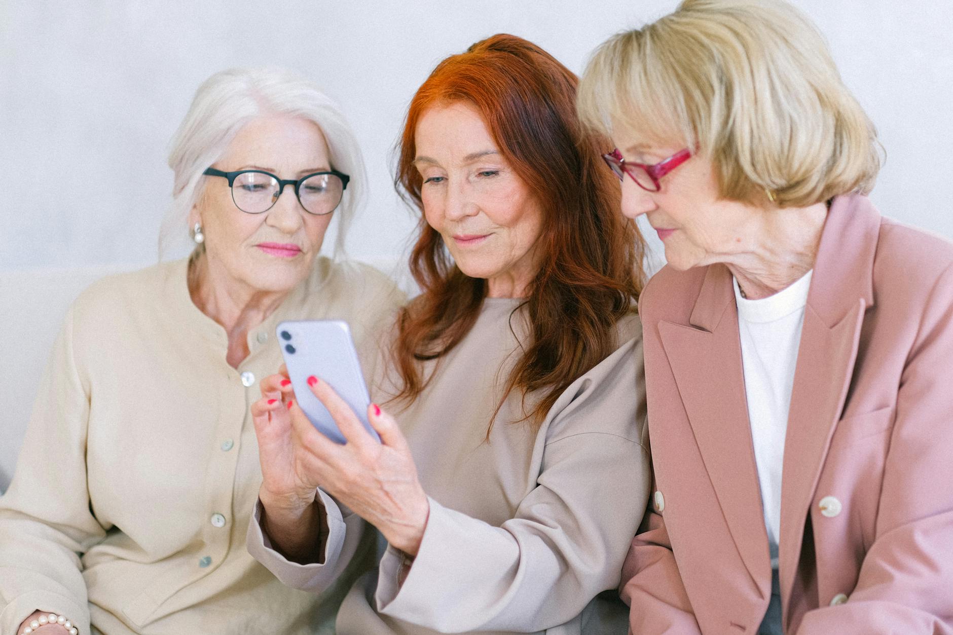 Dwie seniorki w eleganckich strojach uczą się obsługi smartfona