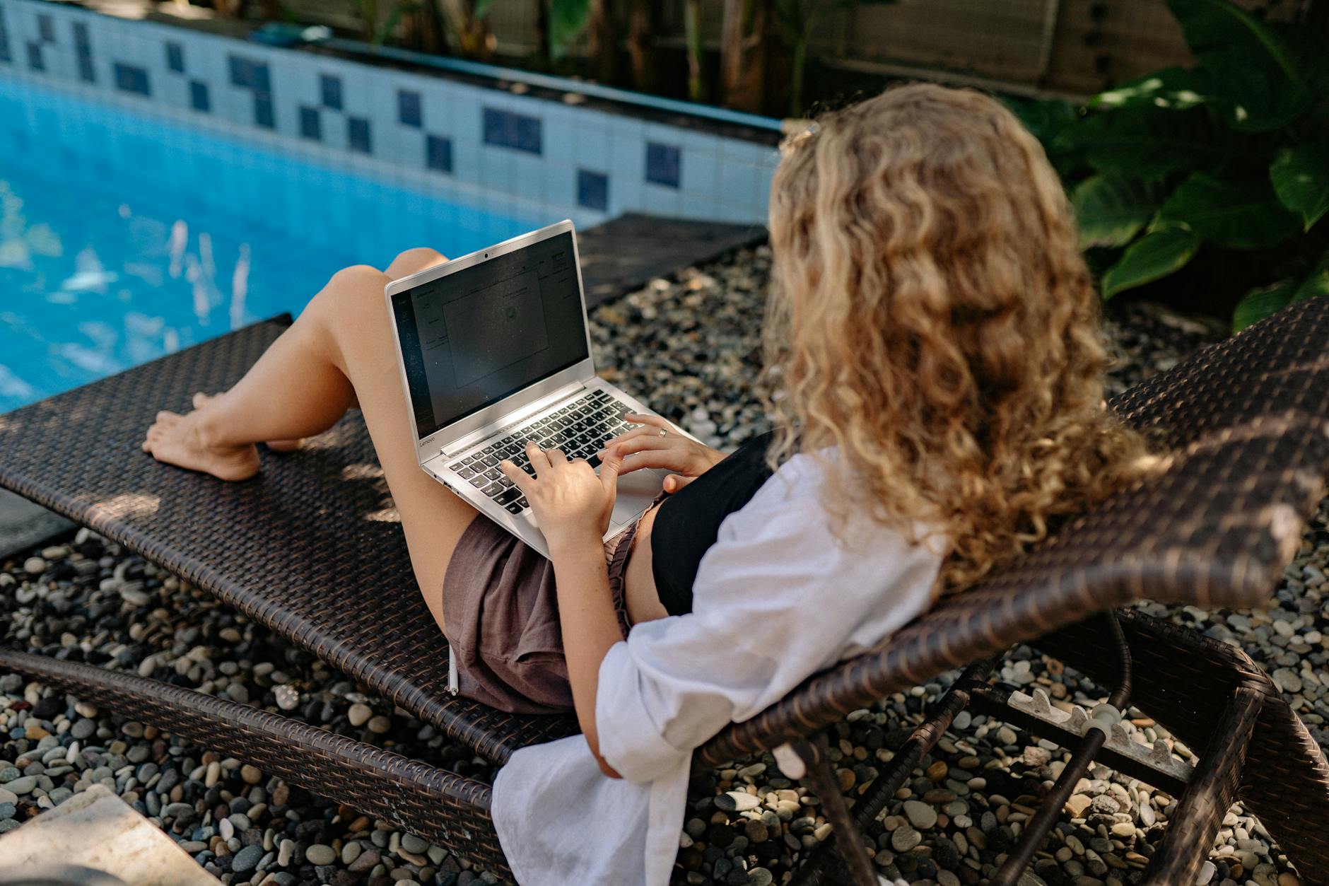 Kobieta pracuje na laptopie przy basenie podczas podróży zawodowej