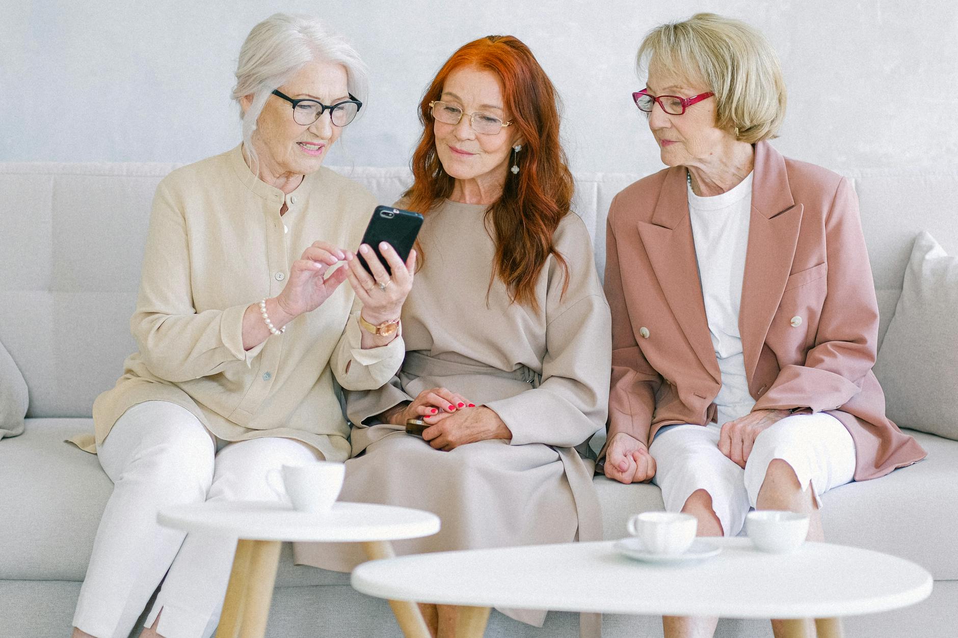 Trzy seniorki na kanapie wspólnie uczą się obsługi smartfona