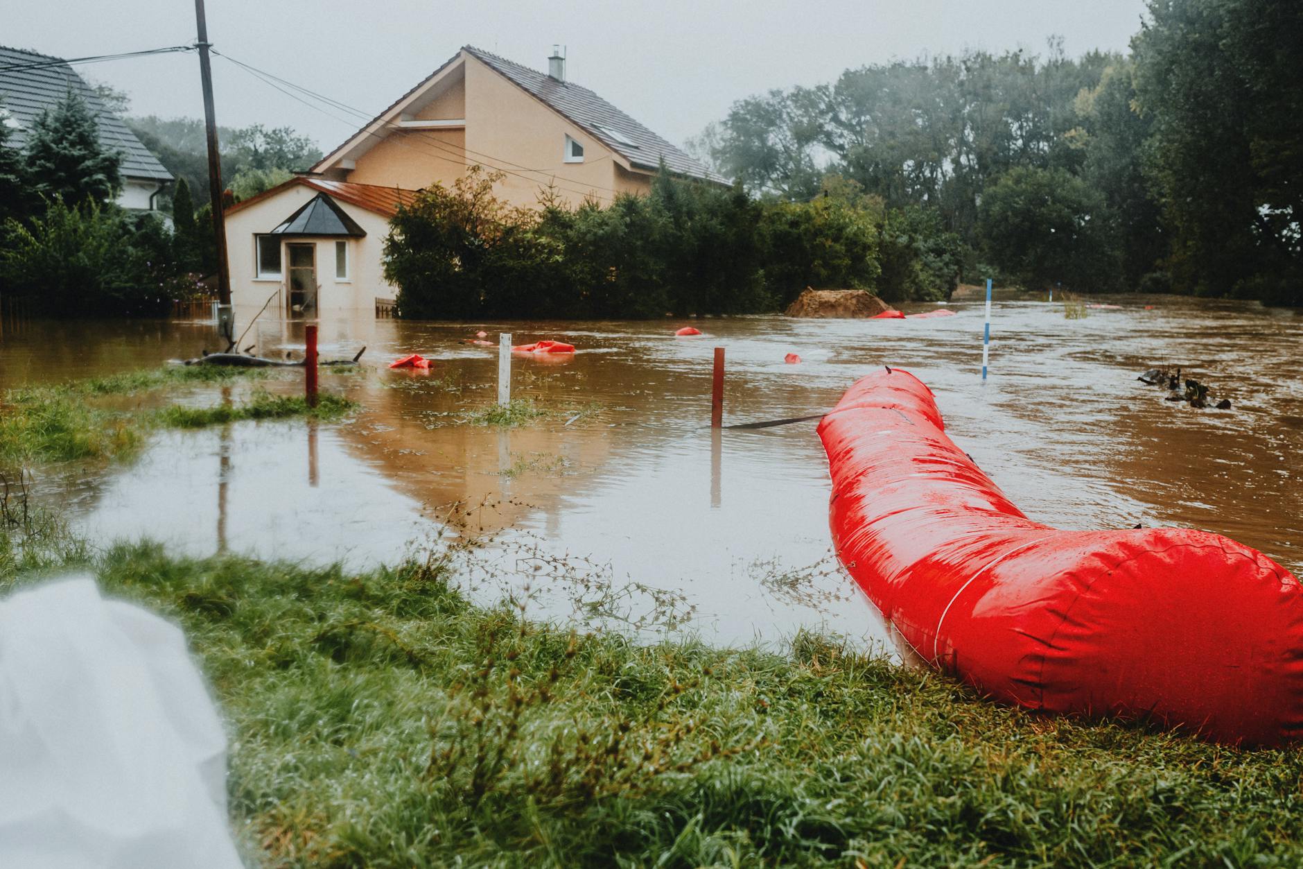 Zalania piwnic w Wejherowie: proste zabezpieczenia, które warto wdrożyć Zalana ulica z domami jednorodzinnymi zabezpieczona czerwonymi barierami