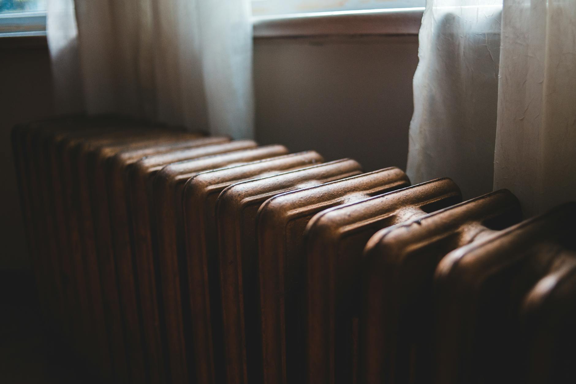 Żeliwny grzejnik pod oknem z zasłonami w domu