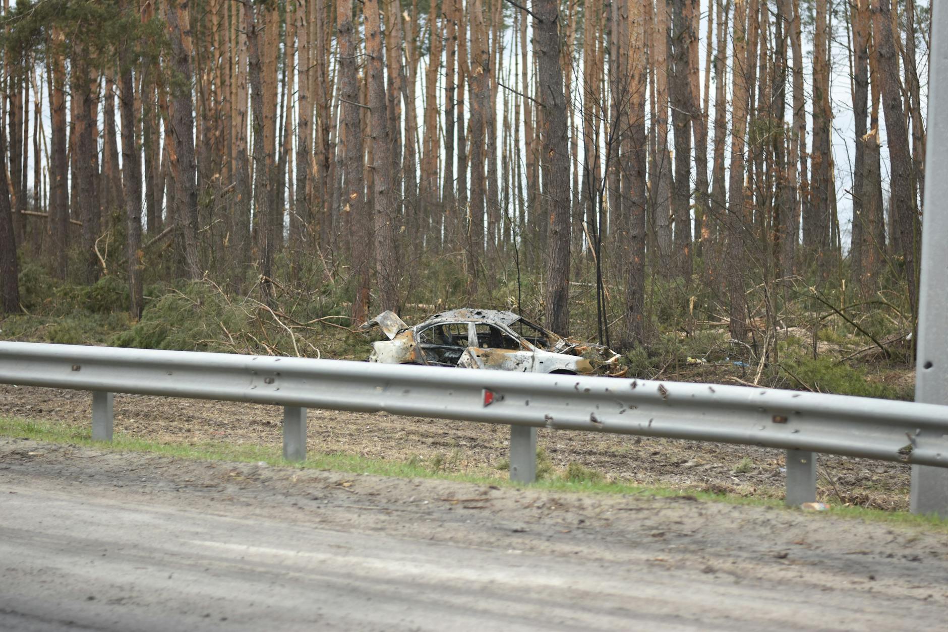Spalone auto po wypadku przy leśnej drodze za metalową barierą