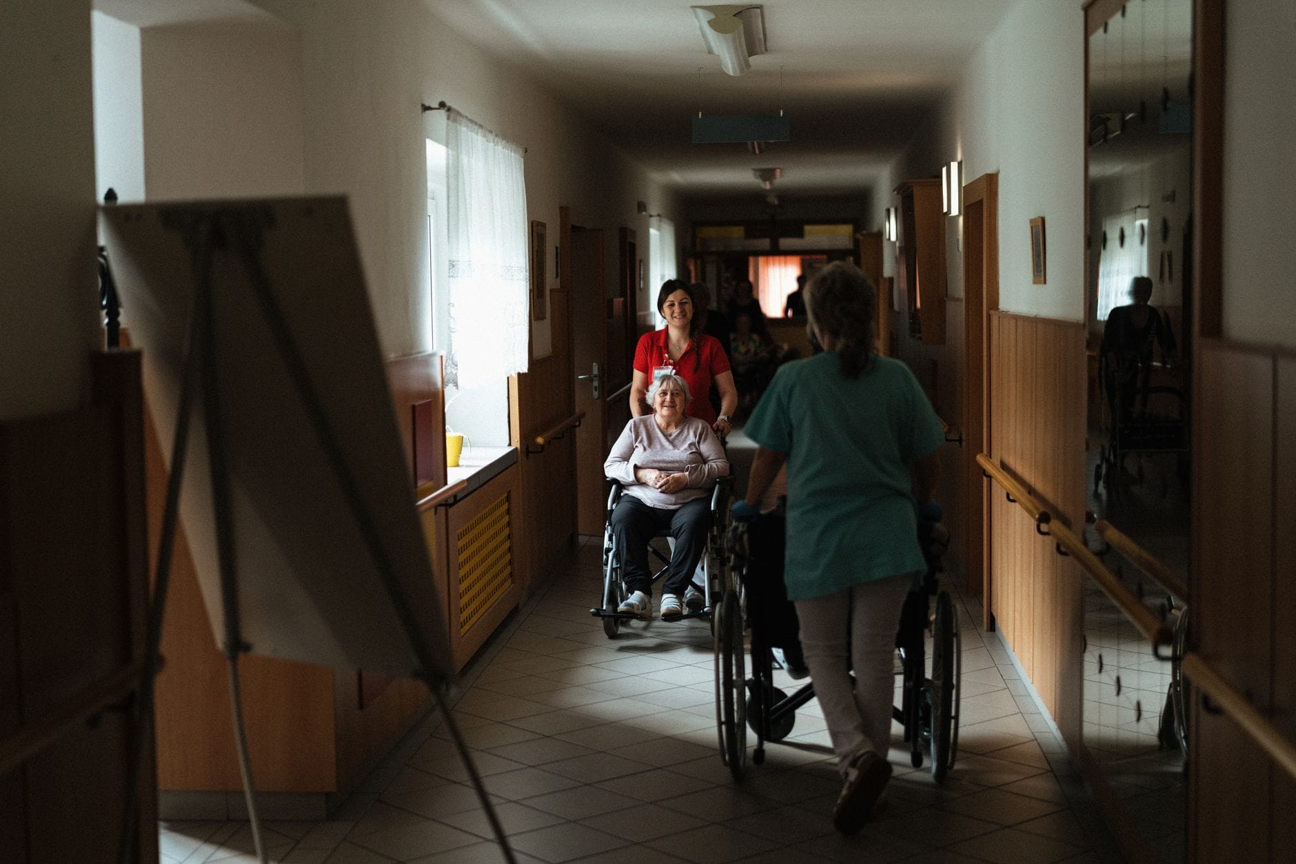 Opiekun prowadzi seniorkę na wózku korytarzem domu opieki