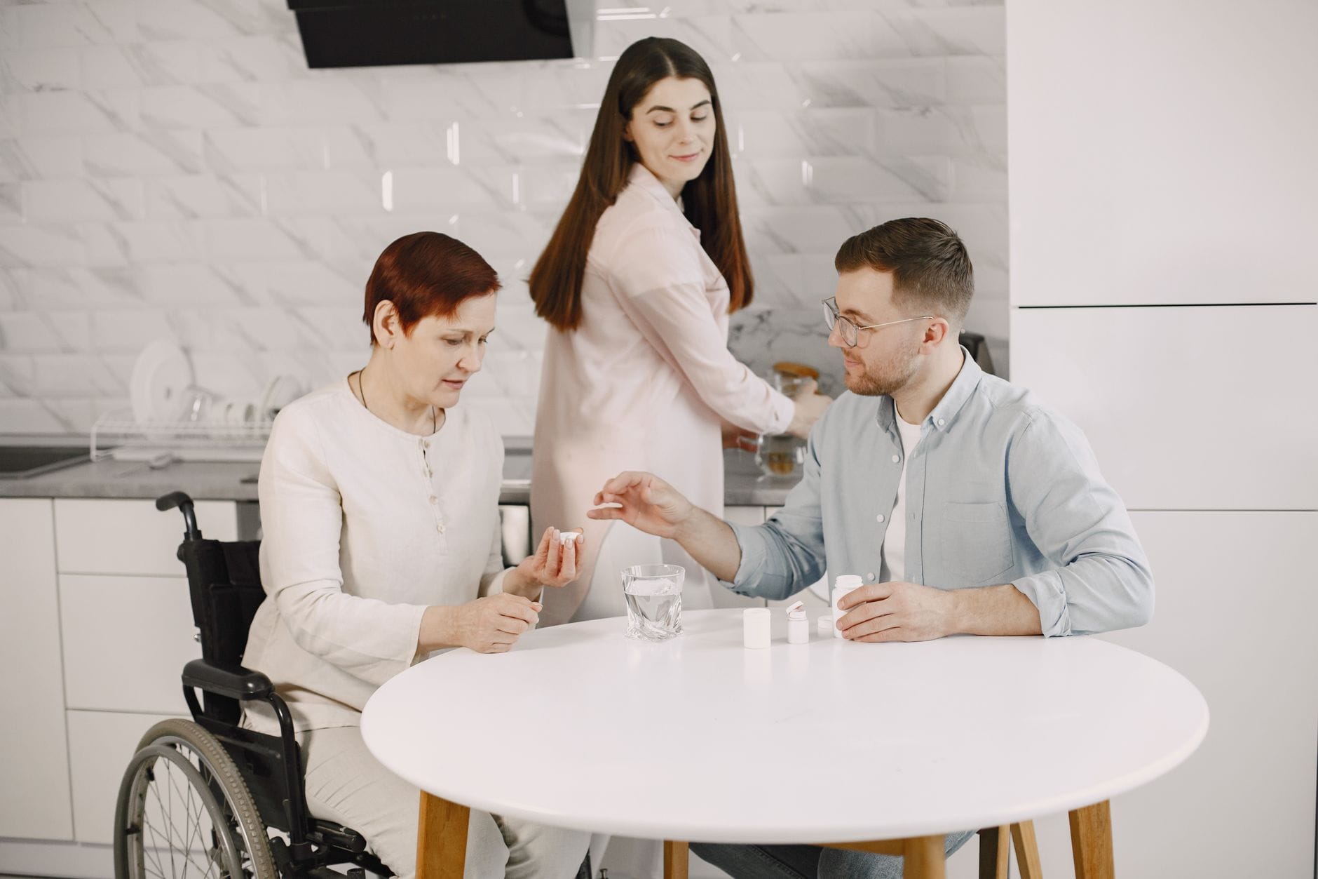 Opiekunka podaje leki starszej kobiecie na wózku w kuchni Opiekunka podaje leki starszej kobiecie na wózku w kuchni